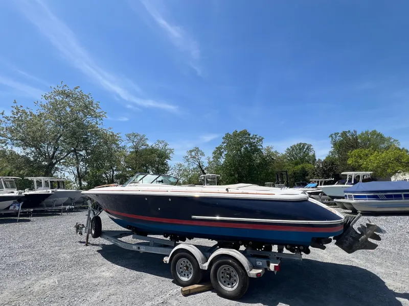 Slide: The Image of 2004 Chris-Craft Corsair 25 boat on trailer, parked outdoors under clear blue sky. - 1