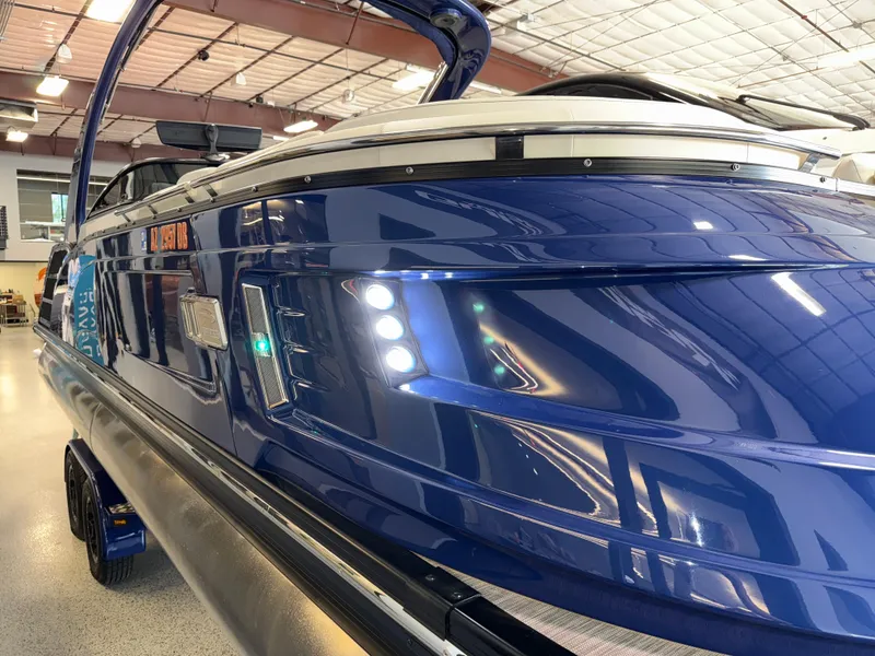 Slide: The Image of 2021 Bennington QX25 boat in showroom, featuring sleek blue exterior and modern design. - 13