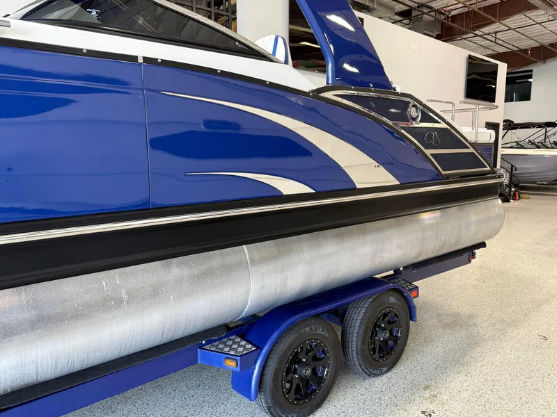 Slide: The Image of 2021 Bennington QX25 pontoon boat in showroom, featuring sleek blue design on trailer. - 3