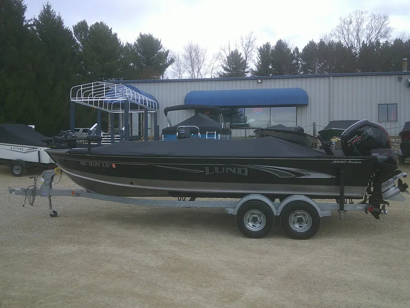 Slide: The Image of 2019 Lund 2000 Alaskan Tiller boat on trailer, parked outdoors near a building. - 19