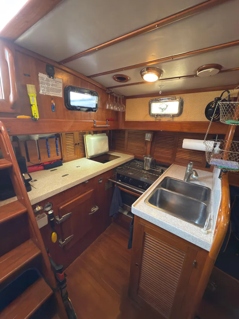 Slide: The Image of 1984 Spindrift Cutter yacht kitchen with wooden cabinetry, stove, and sink. Cozy nautical interior. - 15