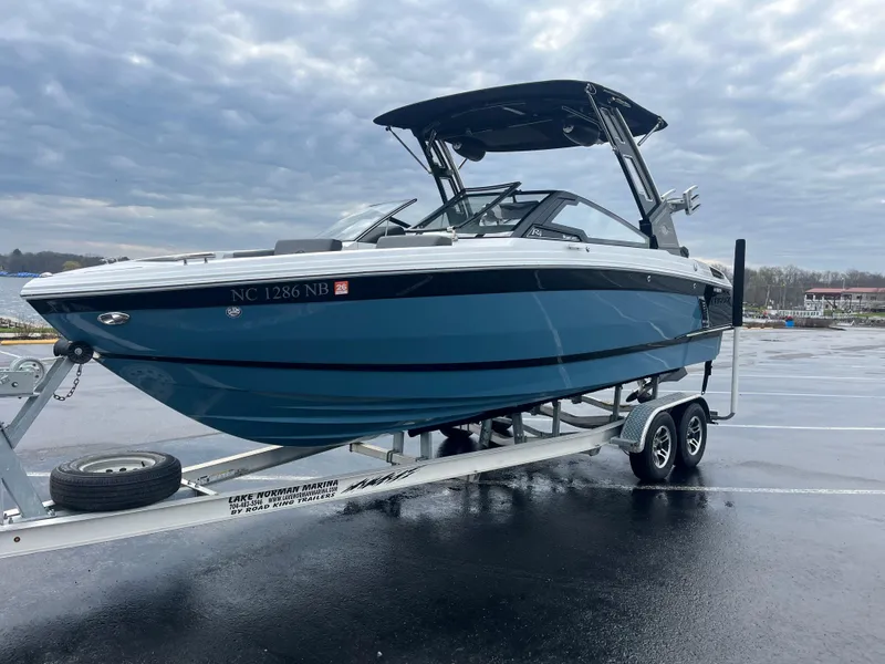 Slide: The Image of 2023 Cobalt R4 Surf boat on trailer, parked on wet pavement under cloudy sky. - 2
