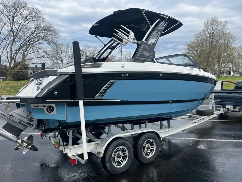 Slide: The Image of 2023 Cobalt R4 Surf boat on trailer, blue and black design, parked outdoors. - 7