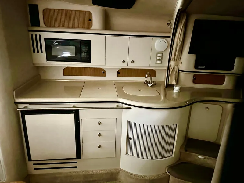 Slide: The Image of 1999 Sea Ray 310 Sundancer interior kitchen with microwave, sink, and storage cabinets. - 18