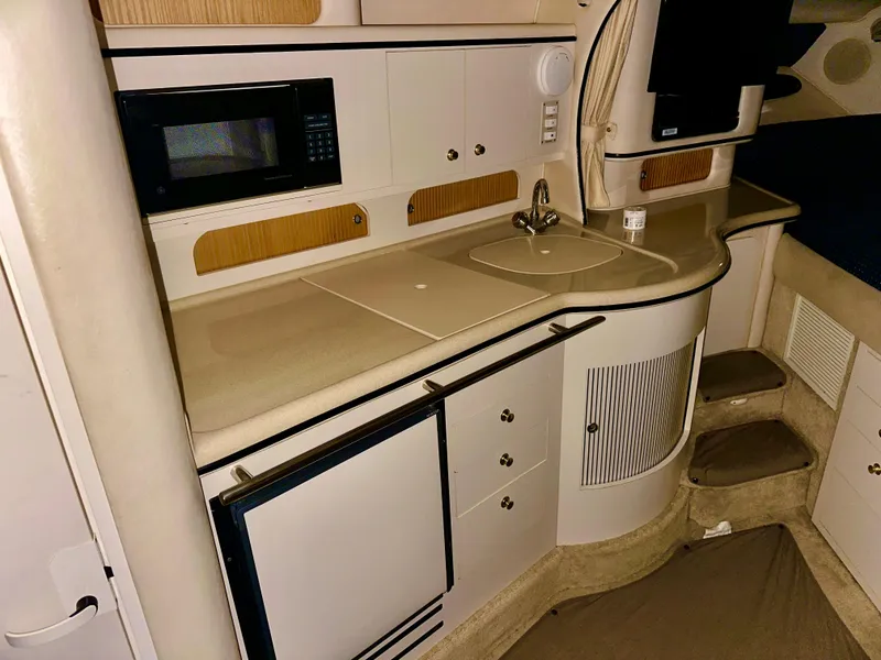 Slide: The Image of 1999 Sea Ray 310 Sundancer interior kitchen with sink, microwave, and storage cabinets. - 19