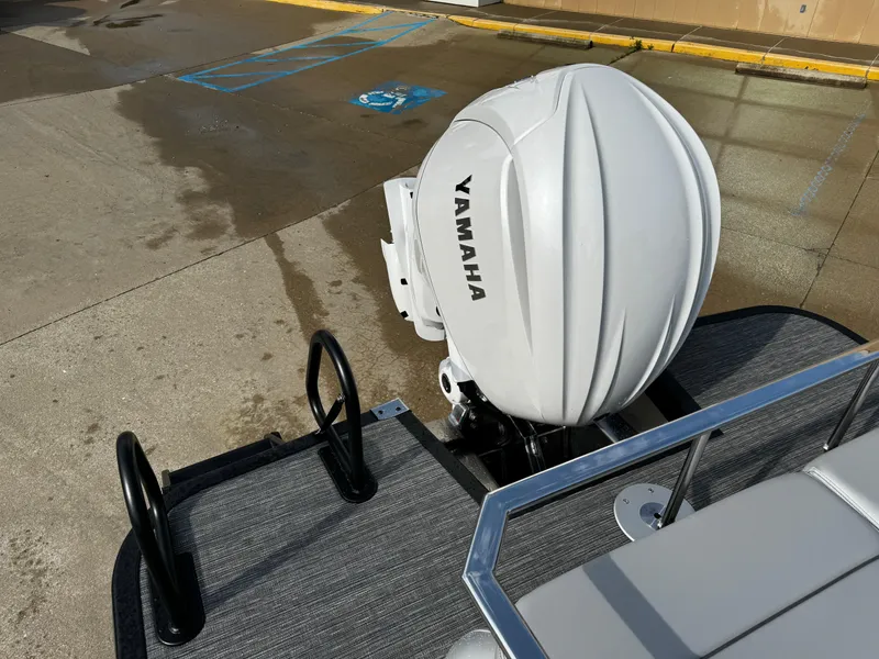 Slide: The Image of 2024 Bennington 25 QXSBA with Yamaha outboard motor, docked on wet pavement. - 21