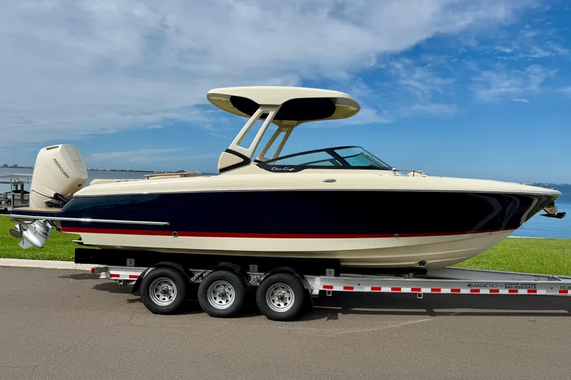 Slide: The Image of 2026 Chris-Craft Sportster 28 boat on trailer, parked by waterfront under blue sky. - 2