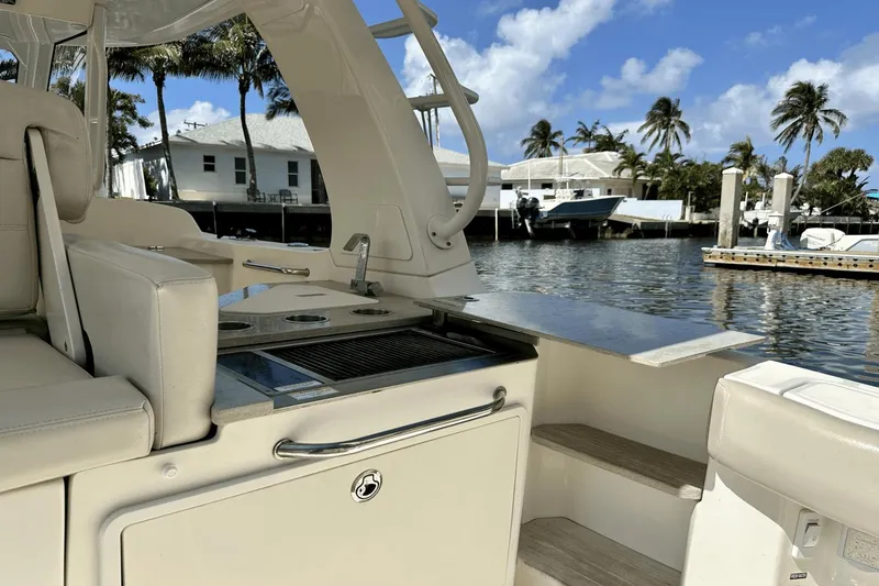 Slide: The Image of 2019 Boston Whaler 350 Realm boat interior with seating and kitchenette, docked by waterfront homes. - 16