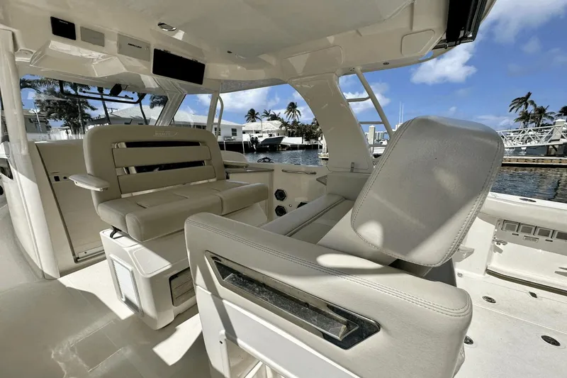 Slide: The Image of 2019 Boston Whaler 350 Realm interior with luxurious seating, docked at a marina under clear skies. - 8