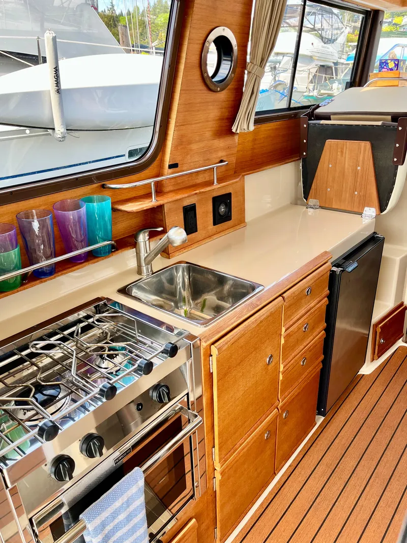Slide: The Image of 2018 Ranger Tugs R-27 interior kitchen with stove, sink, and wooden cabinetry. - 6