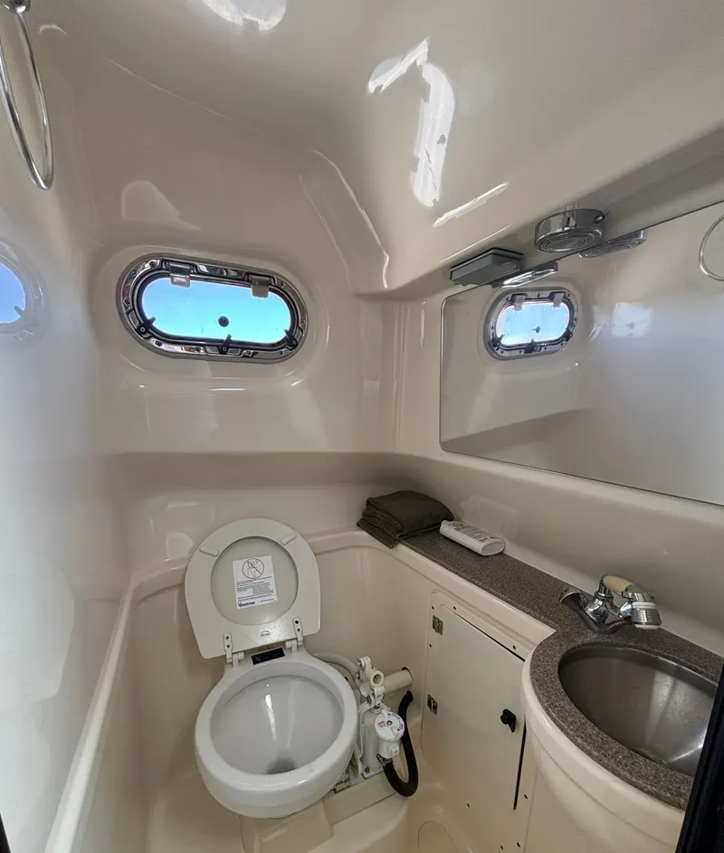 Slide: The Image of 2007 Pursuit 285 Offshore boat bathroom with toilet, sink, and porthole windows. - 24