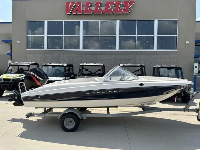 Slide: The Image of 2002 Bayliner 160 Capri boat on trailer outside dealership, with off-road vehicles in background. - 1