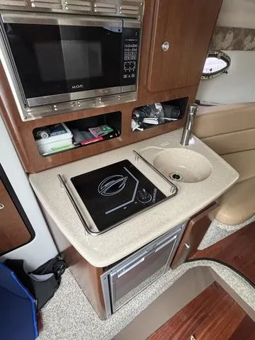 Slide: The Image of 2022 Crownline 264 CR boat interior with kitchenette, featuring a microwave, stove, and sink. - 8