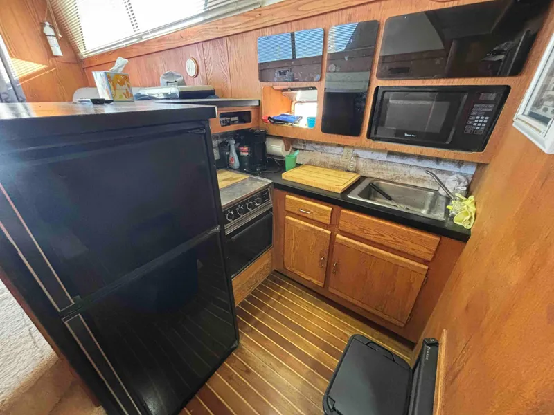 Slide: The Image of 1988 Luhrs Tournament 400 Convertible kitchen with wood cabinets, black appliances, and compact layout. - 9