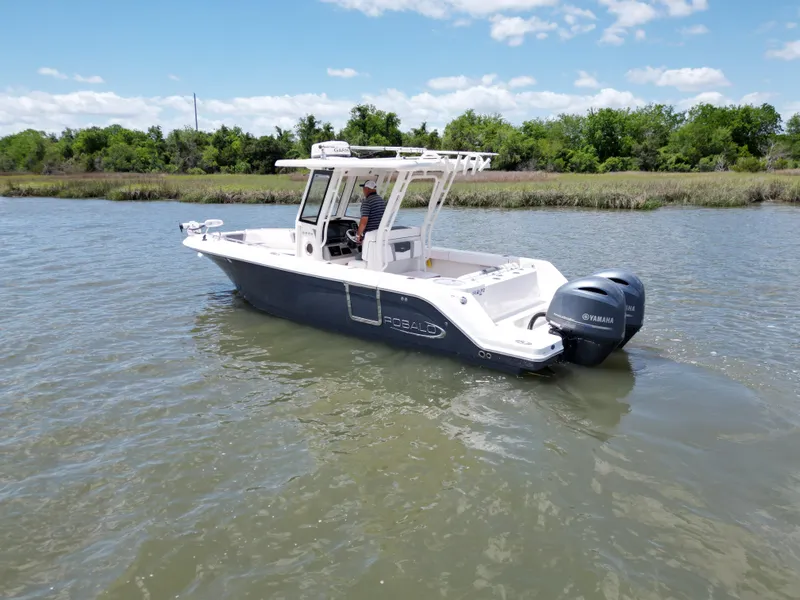 Slide: The Image of 2020 Robalo R272 Center Console boat on calm water, clear sky, and lush greenery. - 4