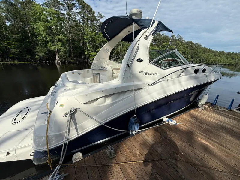 Slide: The Image of 2004 Sea Ray 320 Sundancer docked by a serene forested riverbank. - 0