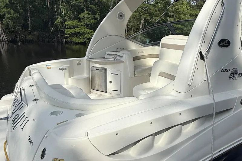 Slide: The Image of 2004 Sea Ray 320 Sundancer boat with white seating and sleek design, docked near lush greenery. - 2