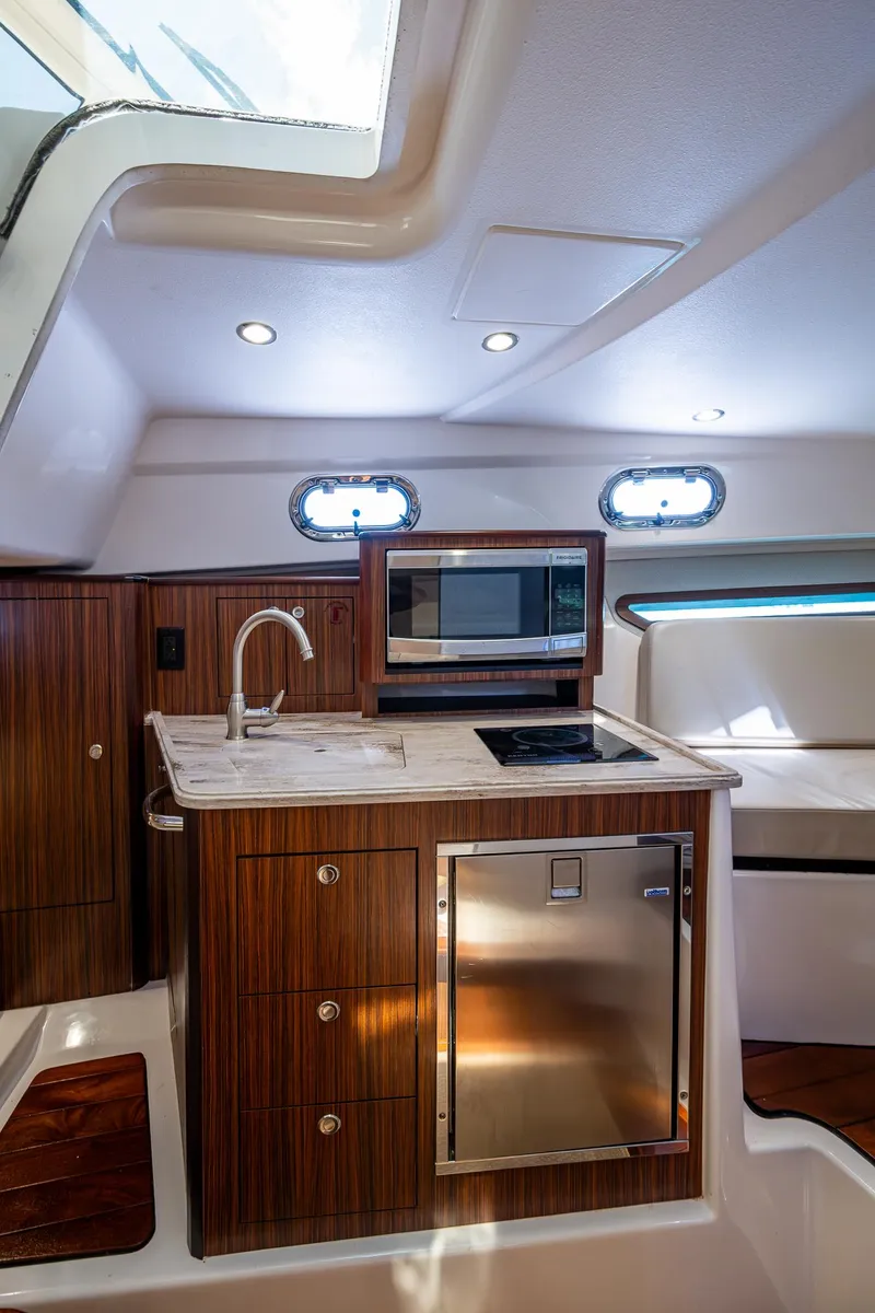 Slide: The Image of 2017 Pursuit 325 OS yacht interior with kitchenette, featuring wood cabinetry, sink, and microwave. - 14