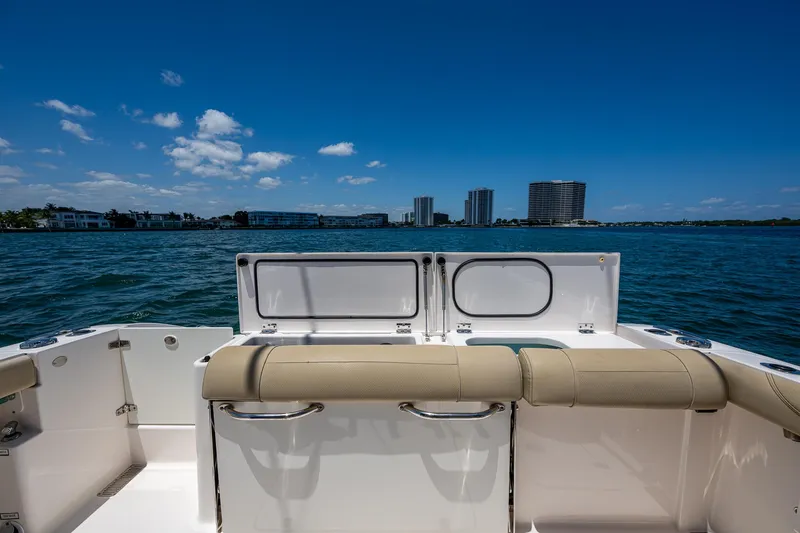 Slide: The Image of 2017 Pursuit 325 OS boat with beige seating, ocean view, and city skyline in the background. - 18