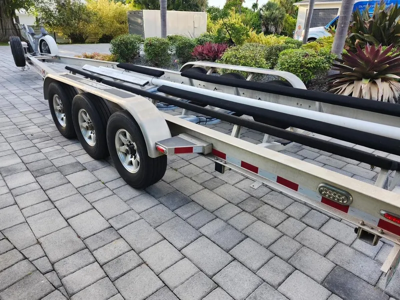 Slide: The Image of Triple-axle boat trailer on paved driveway, surrounded by lush greenery. - 41