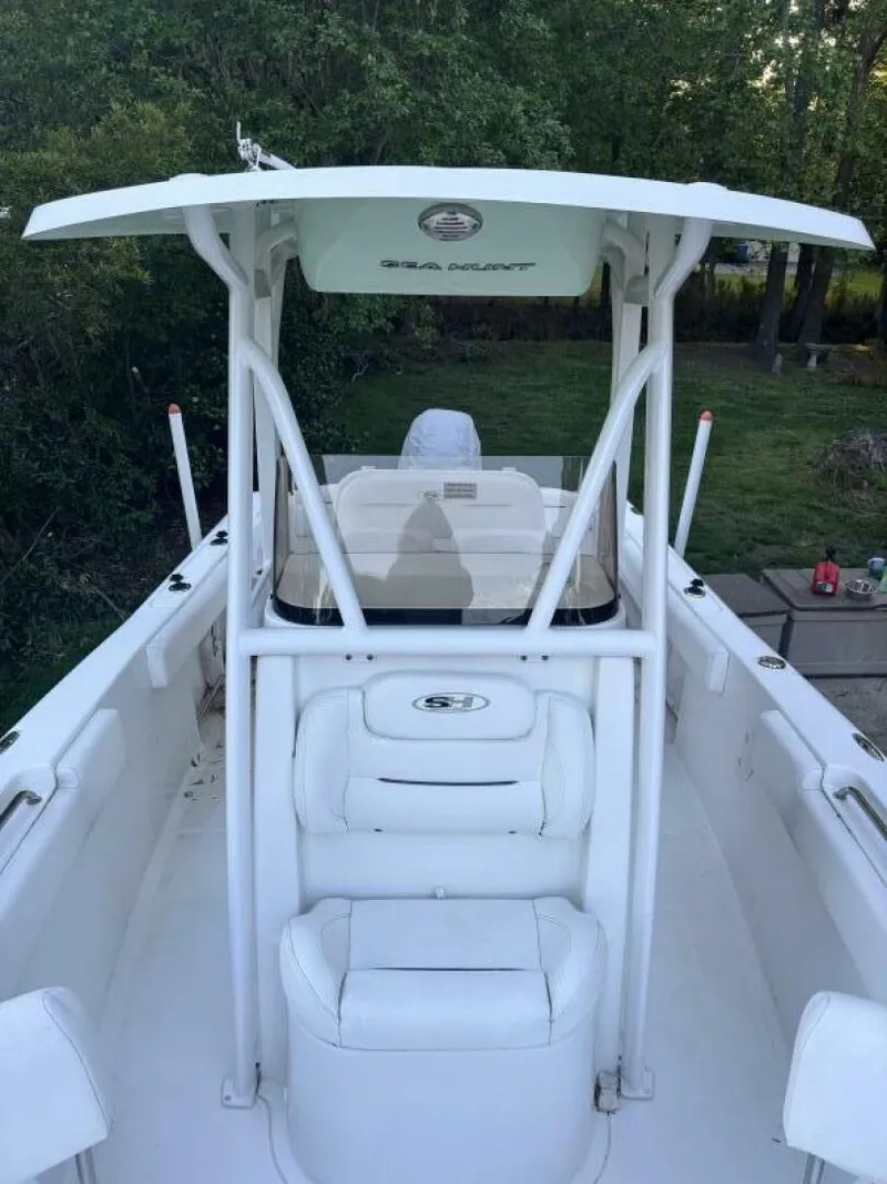 Slide: The Image of 2017 Sea Hunt Ultra 225 boat with T-top and seating, docked near greenery. - 18