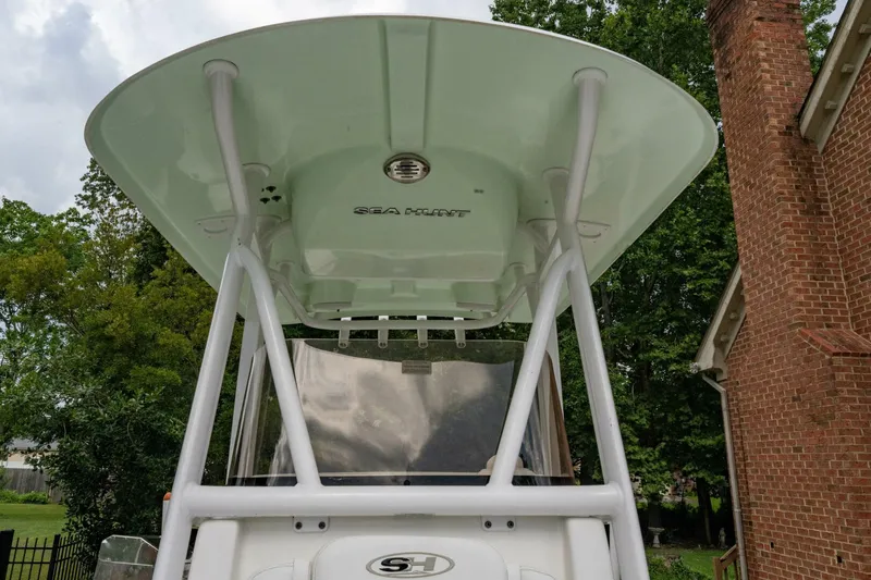 Slide: The Image of 2017 Sea Hunt Ultra 225 boat with T-top, parked near brick building and trees. - 6