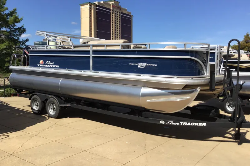 The Image of 2025 Sun Tracker Fishin' Barge 22 DLX pontoon boat on trailer, parked outdoors. - 0