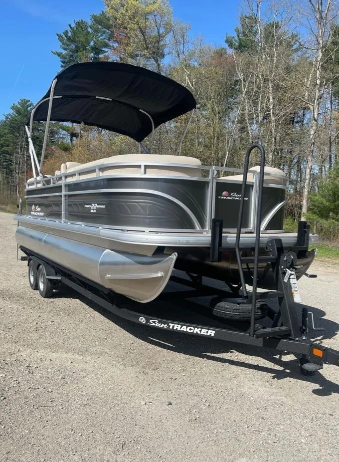 Slide: The Image of 2025 Sun Tracker Party Barge 22 DLX pontoon boat on trailer, parked outdoors. - 2