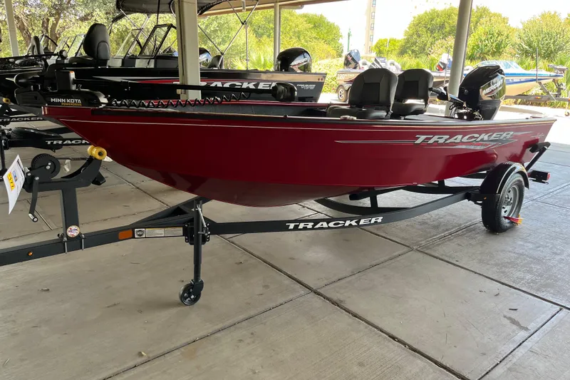 The Image of 2025 Tracker Super Guide V-16 T boat on trailer, red hull, parked under shelter. - 0