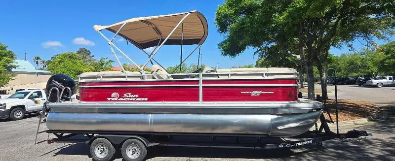 Slide: The Image of 2025 Sun Tracker Party Barge 22 RF DLX pontoon boat on trailer, parked outdoors. - 2