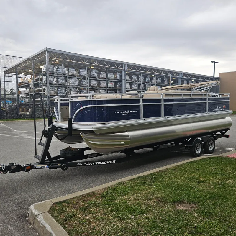Slide: The Image of 2025 Sun Tracker Fishin' Barge 22 DLX pontoon boat on trailer in parking lot. - 2