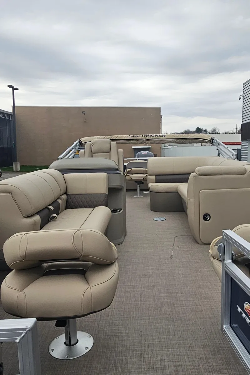 Slide: The Image of 2025 Sun Tracker Fishin' Barge 22 DLX with beige seating, spacious deck, and overcast sky. - 4