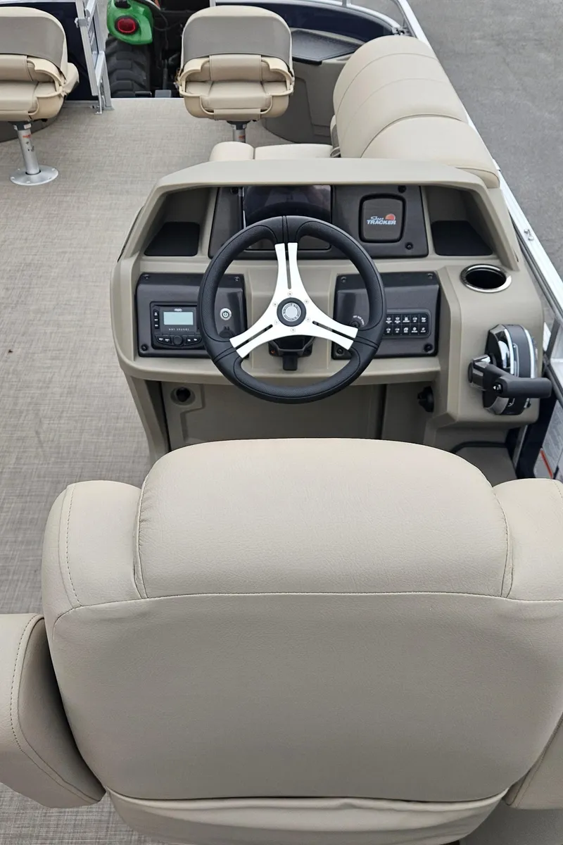 Slide: The Image of 2025 Sun Tracker Fishin' Barge 22 DLX boat interior with steering wheel and beige seating. - 5