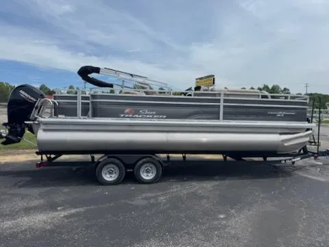 The Image of 2025 Sun Tracker Fishin' Barge 22 DLX pontoon boat on trailer, parked outdoors. - 0