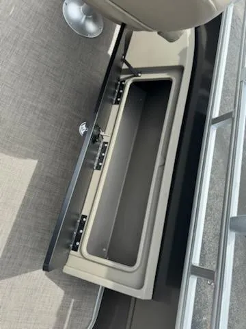 Slide: The Image of 2025 Sun Tracker Fishin' Barge 22 DLX storage compartment with beige interior and metal railing. - 12