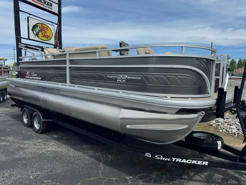 Slide: The Image of 2025 Sun Tracker Fishin' Barge 22 DLX pontoon boat on trailer in parking lot. - 2