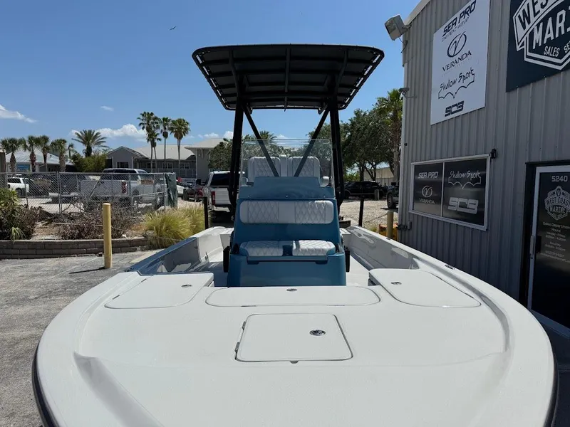 Slide: The Image of 2025 Shallow Sport 24 Modified V boat with T-top, parked near a marina building. - 3