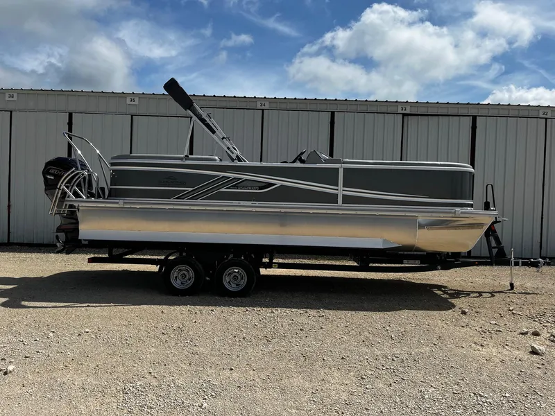 The Image of 2025 SunCatcher Fusion 324RC pontoon boat on trailer, parked outdoors under a cloudy sky. - 0