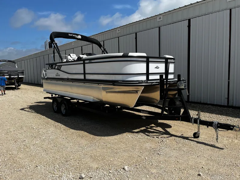 Slide: The Image of 2025 SunCatcher Select 322SS pontoon boat on trailer, parked outdoors near storage units. - 1