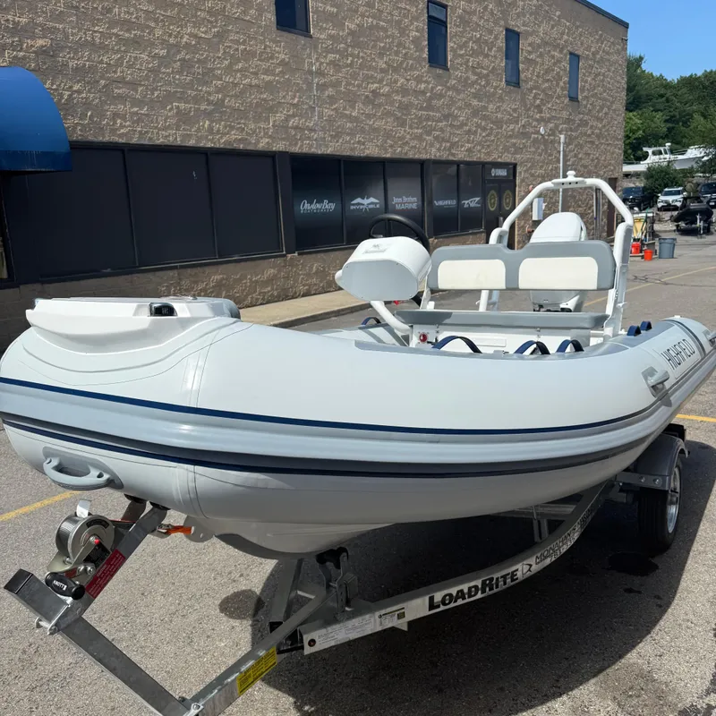 Slide: The Image of 2025 Highfield CL400 inflatable boat on trailer, parked outside a marine store. - 1