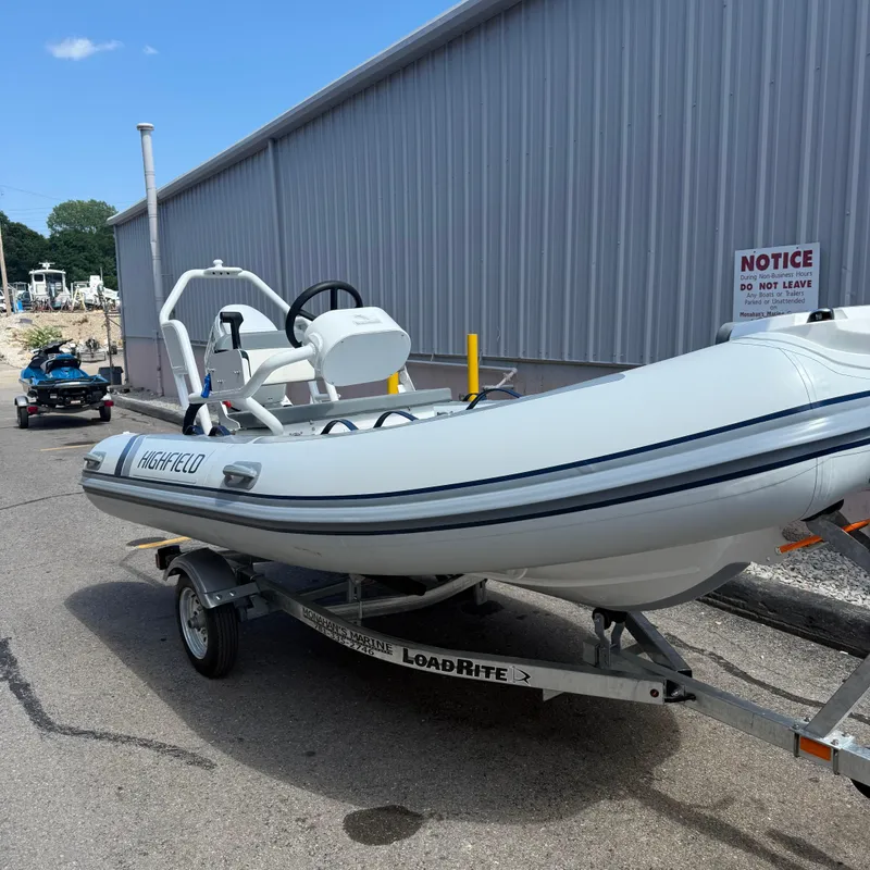 Slide: The Image of 2025 Highfield CL400 inflatable boat on trailer, parked near industrial building. - 2