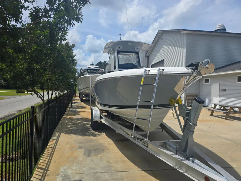 Slide: The Image of 2025 Pursuit S 248 Sport boat on trailer, parked outdoors near a building. - 2