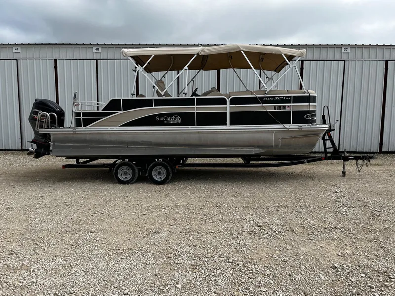 The Image of 2016 SunCatcher Elite 324 RS pontoon boat on trailer, parked outdoors. - 0