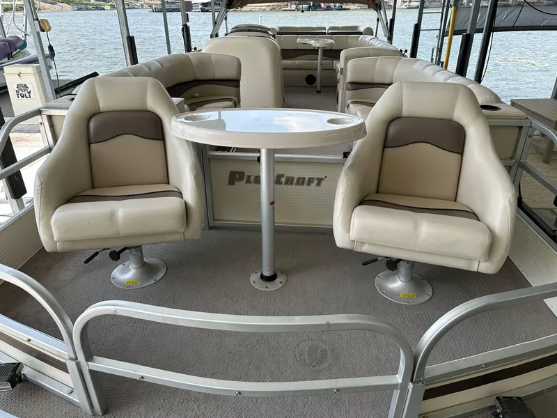 Slide: The Image of 2004 PlayCraft 2500 Ultra pontoon boat interior with seating and table, docked by the water. - 35
