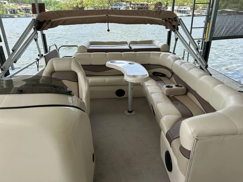Slide: The Image of 2004 PlayCraft 2500 Ultra pontoon boat interior with beige seating and table, docked by the lake. - 5