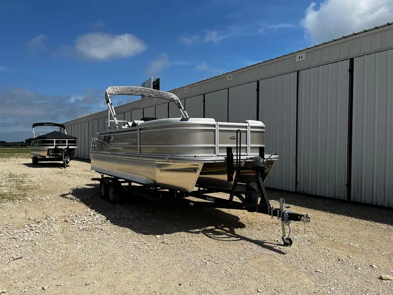 Slide: The Image of 2025 SunCatcher Select 324SL pontoon boat on trailer, parked near storage facility. - 1