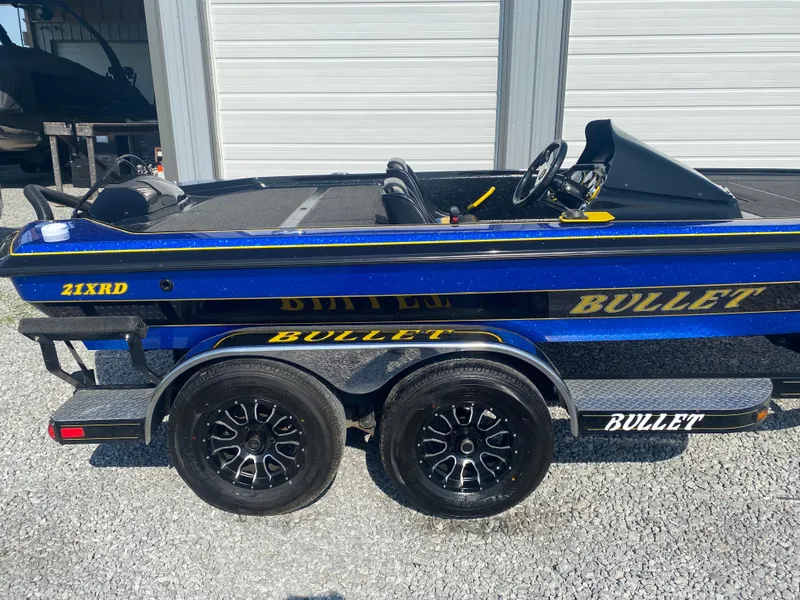 Slide: The Image of 2013 Bullet 21XRD boat with dual-axle trailer, parked on gravel. - 4