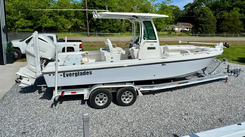 Slide: The Image of 2019 Everglades 253CC boat on trailer, parked on gravel, surrounded by greenery. - 5