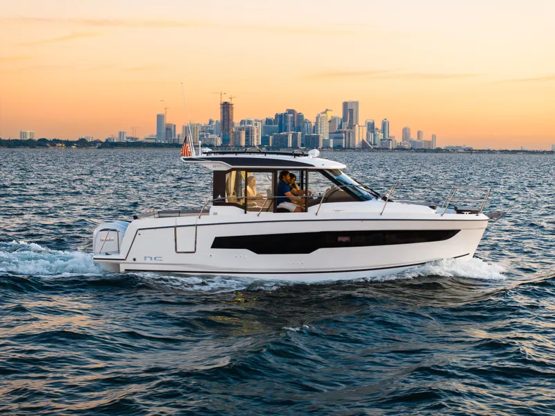 Slide: The Image of 2025 Jeanneau NC895 S2 cruising on water with city skyline at sunset. - 2