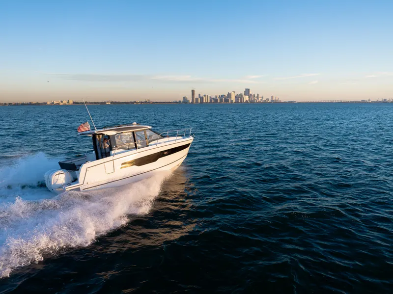 Slide: The Image of 2025 Jeanneau NC895 S2 cruising on open water with city skyline in background. - 3